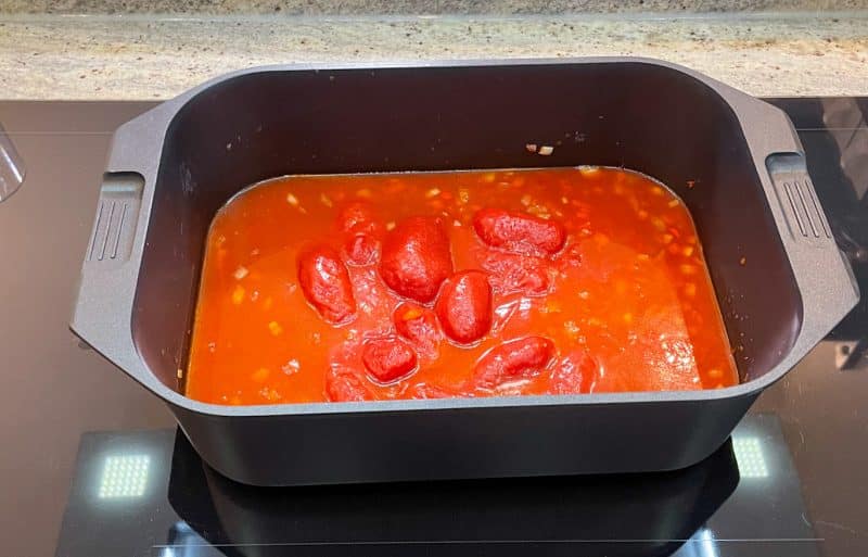 Sauce zubereiten: In einem großen Topf oder Bräter etwas Öl erhitzen. Die gewürfelte Zwiebel darin anbraten. Die fein gewürfelte Paprika hinzufügen und kurz mit anbraten. Tomatenmark und Paprikamark hinzufügen und kurz mitbraten. Mit Rinderfond ablöschen und die geschälten Tomaten hinzufügen.