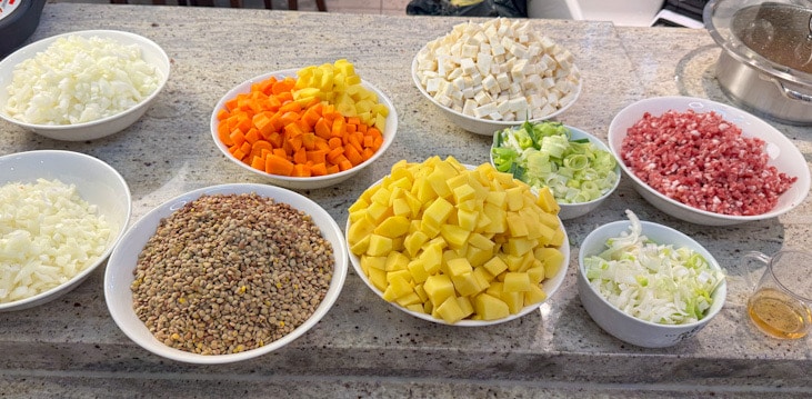 Geschnittene Zutaten für Linsensuppe – Karotten, Kartoffeln, Sellerie, Zwiebeln und Tellerlinsen in Schalen vorbereitet