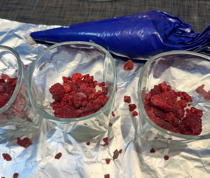 Creme und gefrorene Himbeeren werden abwechselnd in Gläser geschichtet