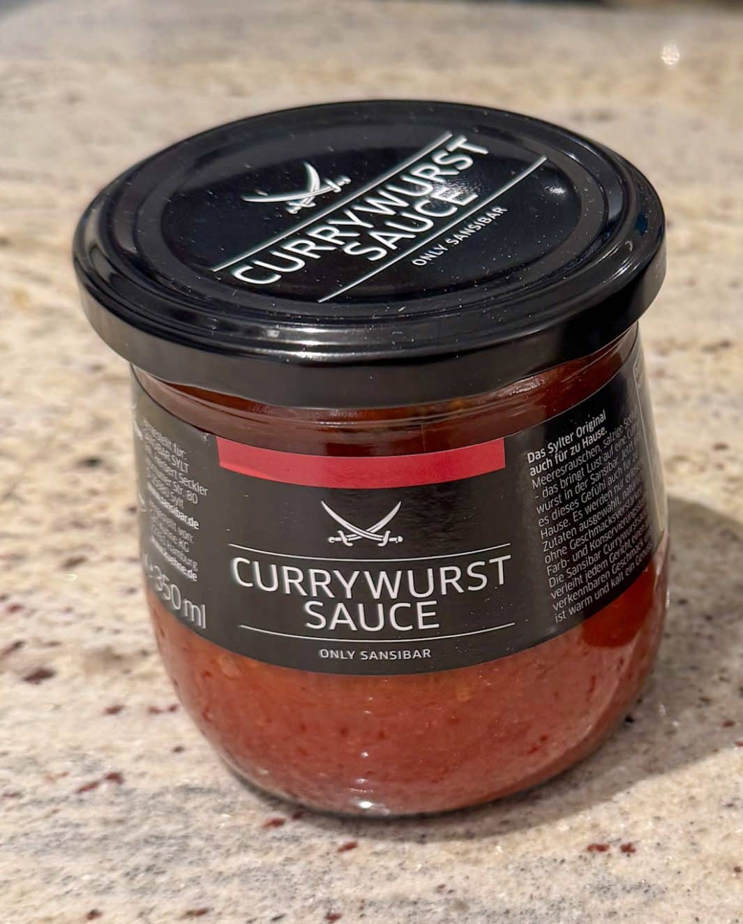 Glas Sansibar Currywurst Sauce mit schwarzem Deckel und Logo auf Marmortisch