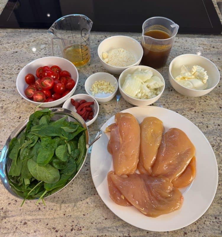 Frische Zutaten wie Spinat, Hähnchenbrust, Tomaten und Zwiebeln auf einer Küchenarbeitsplatte