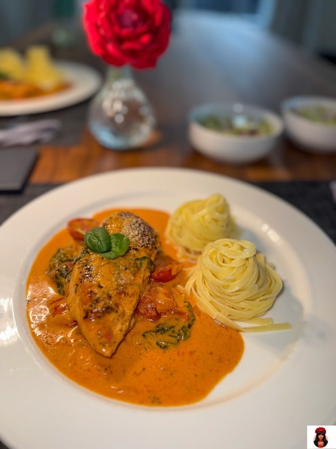 Hähnchenbrust in cremiger Parmesan-Sauce mit Spinat, serviert mit Pasta auf einem weißen Teller