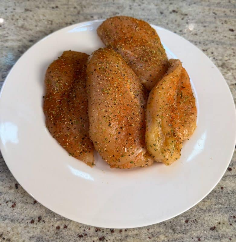 Gewürzte Hähnchenbrustfilets auf einem weißen Teller, bereit zum Anbraten