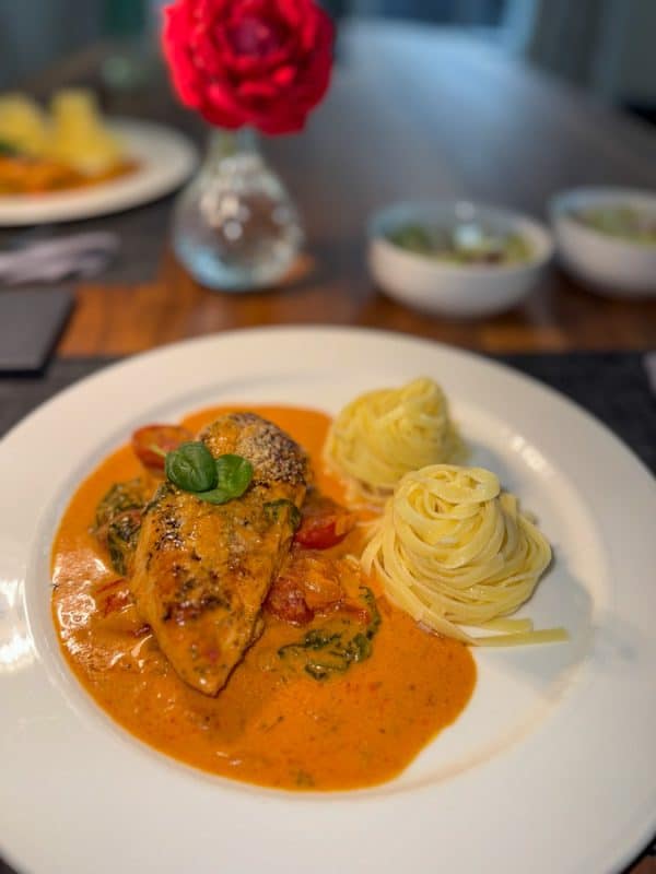 Hähnchenbrust in cremiger Parmesan-Sauce mit Spinat, serviert mit Pasta auf einem weißen Teller