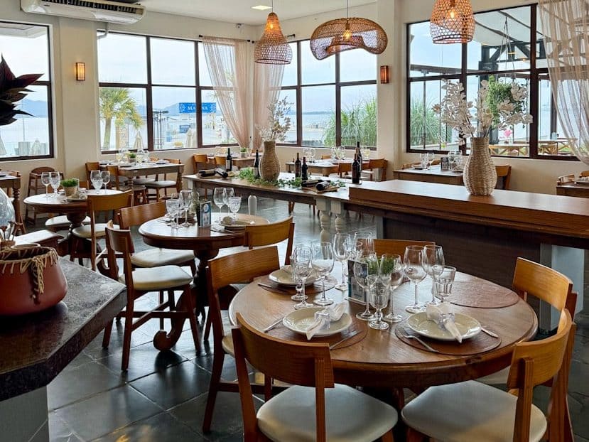 Innenraum des Convés Restaurants in São Francisco do Sul, Brasilien, mit warmem Design, gedeckten Tischen und großen Fenstern zum Meer.