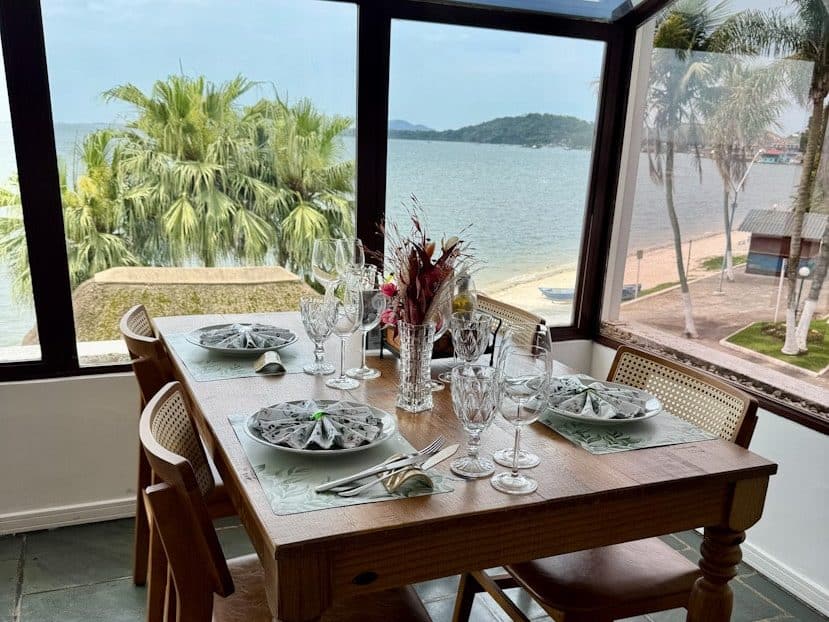 Gedeckter Tisch im ersten Stock des Convés Restaurants in São Francisco do Sul, Brasilien, mit Blick auf Meer und Palmen.
